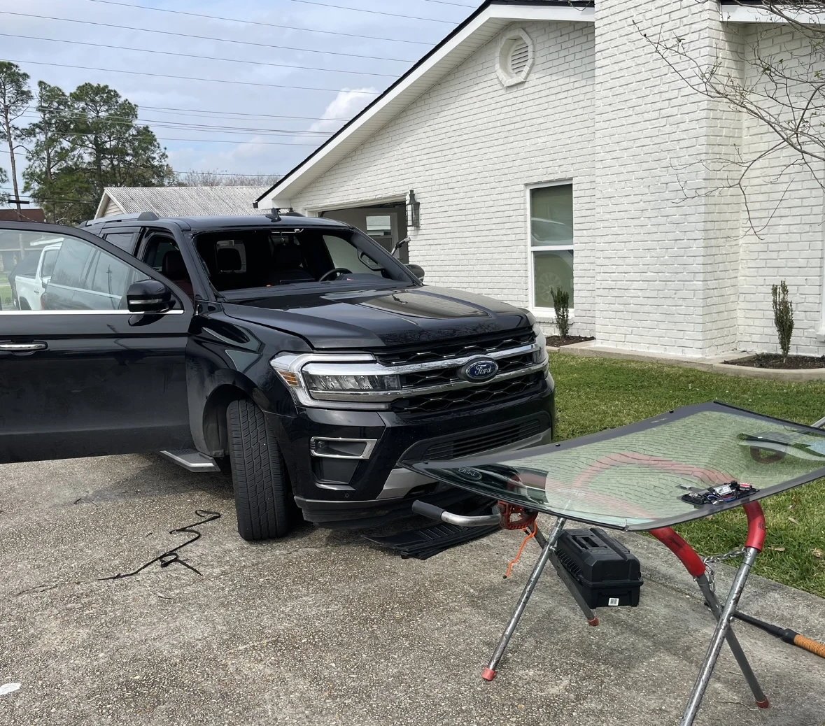 A Ford SUV with its windshield removed during mobile glass service on a residential driveway.